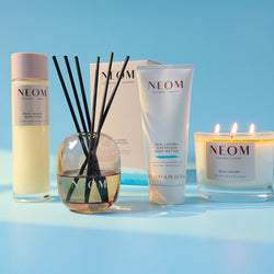 NEOM product range including bath foam, diffuser, body butter, and candle on a blue background