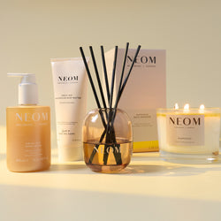NEOM product lineup including a bottle, cream, diffuser, and candle on a light background