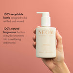 NEOM Great Day Hand Lotion bottle held in hand on coral background, 100% recyclable and natural fragrance skincare