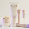 NEOM wellness products including a candle, body butter, sleep pen and pillow mist on a light background.