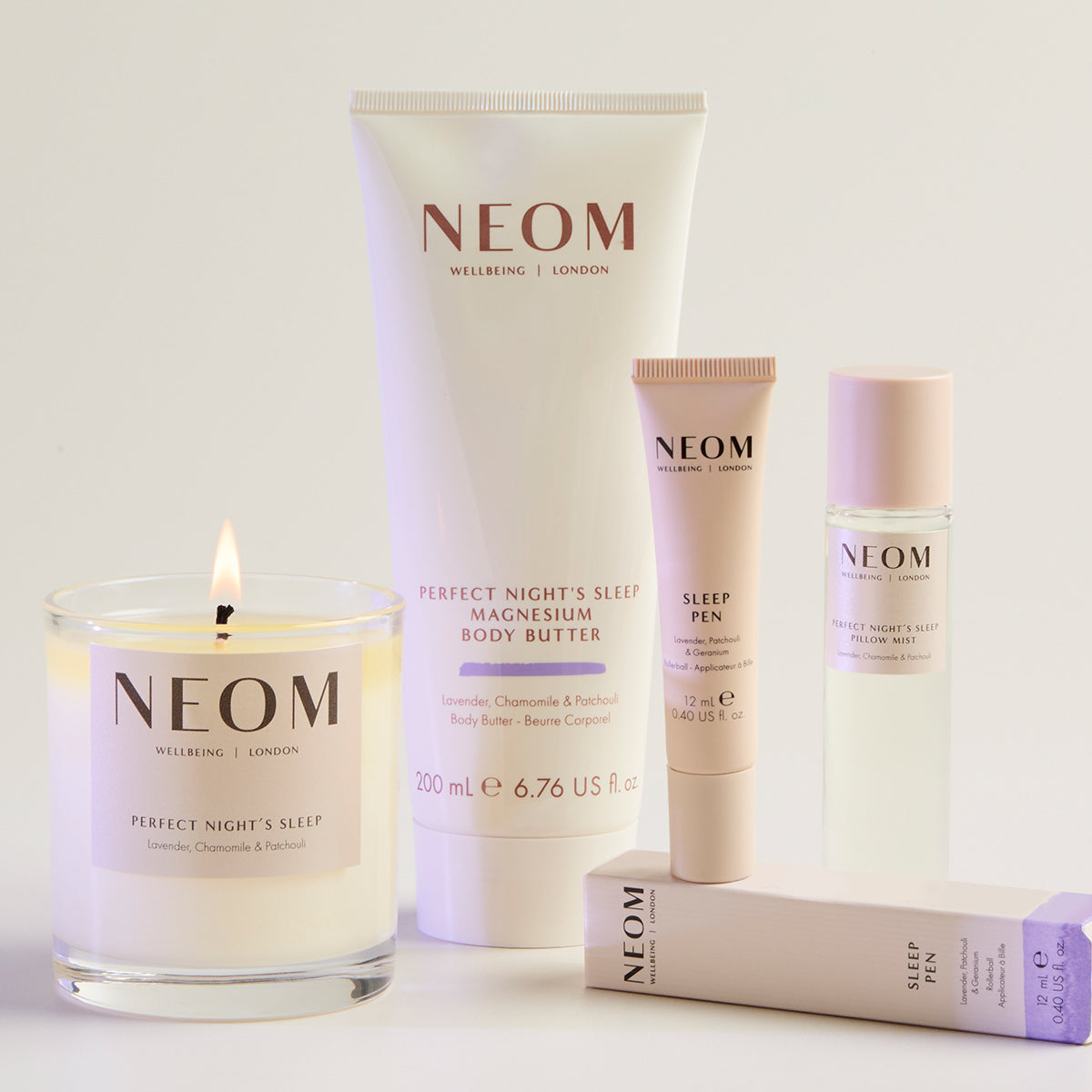 NEOM wellness products including a candle, body butter, sleep pen and pillow mist on a light background.