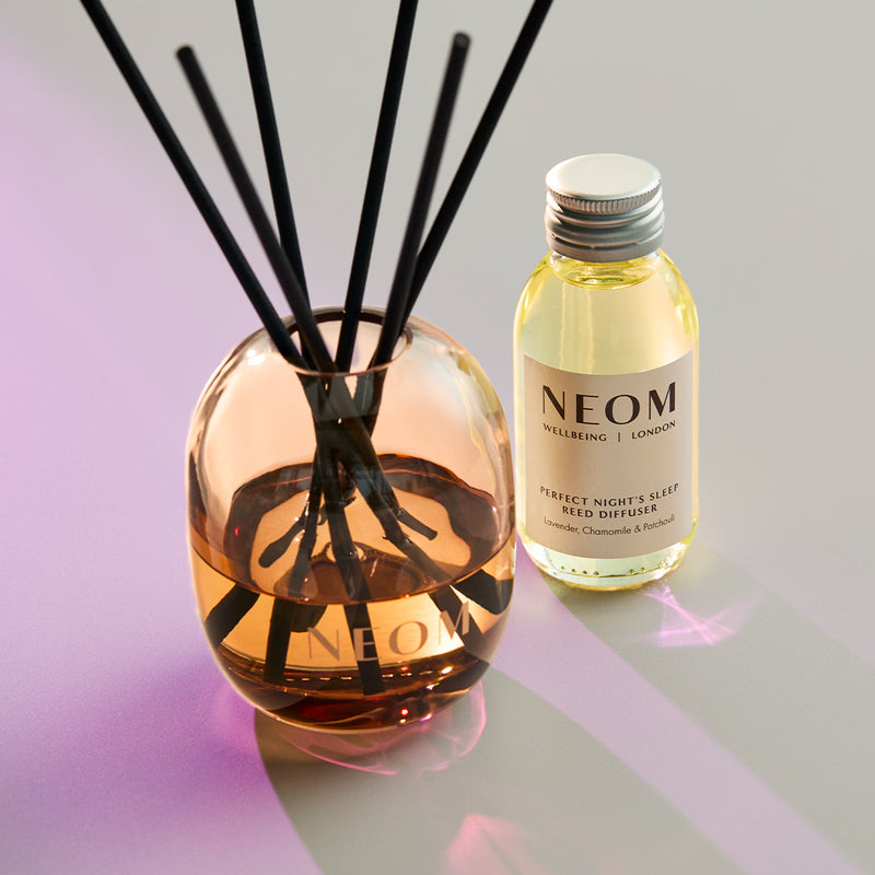 NEOM reed diffuser and bottle on a reflective surface with a gradient background
