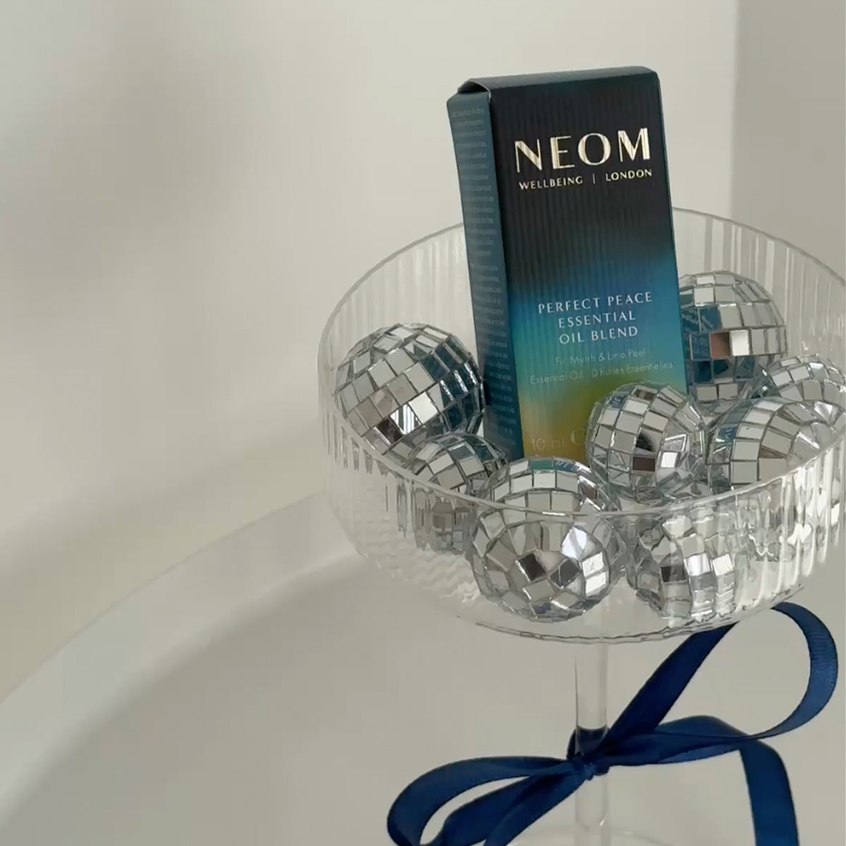 NEOM Perfect Peace Essential Oil Blend box displayed in a glass bowl filled with silver disco balls.