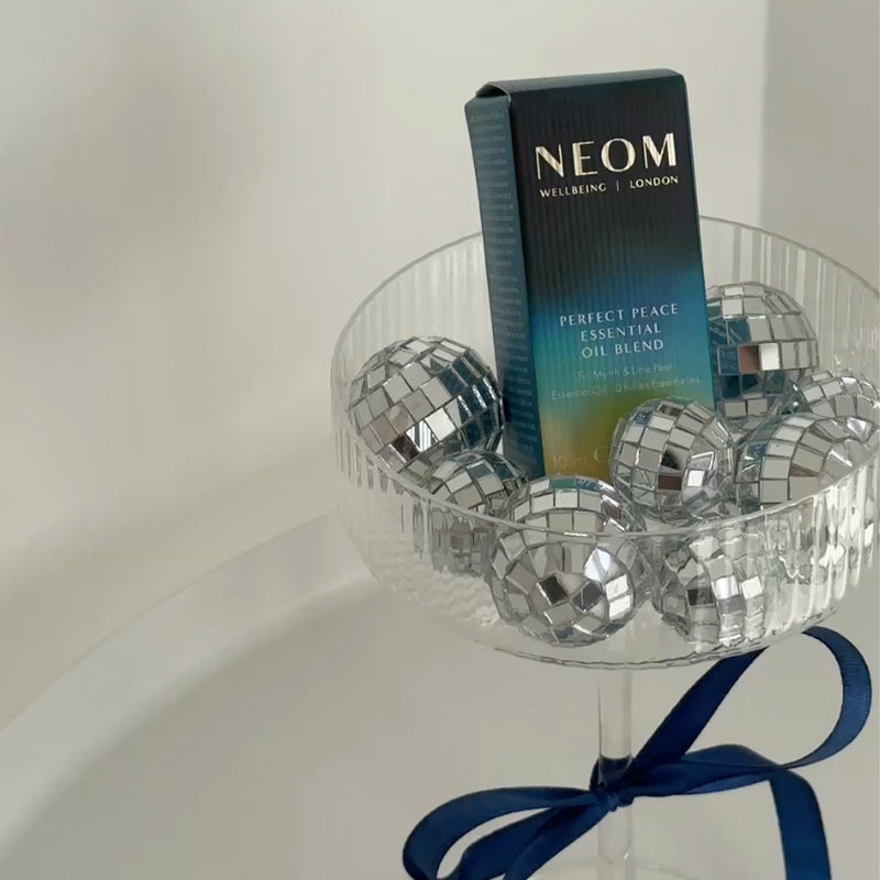 NEOM Perfect Peace Essential Oil Blend box displayed in a glass bowl filled with silver disco balls.