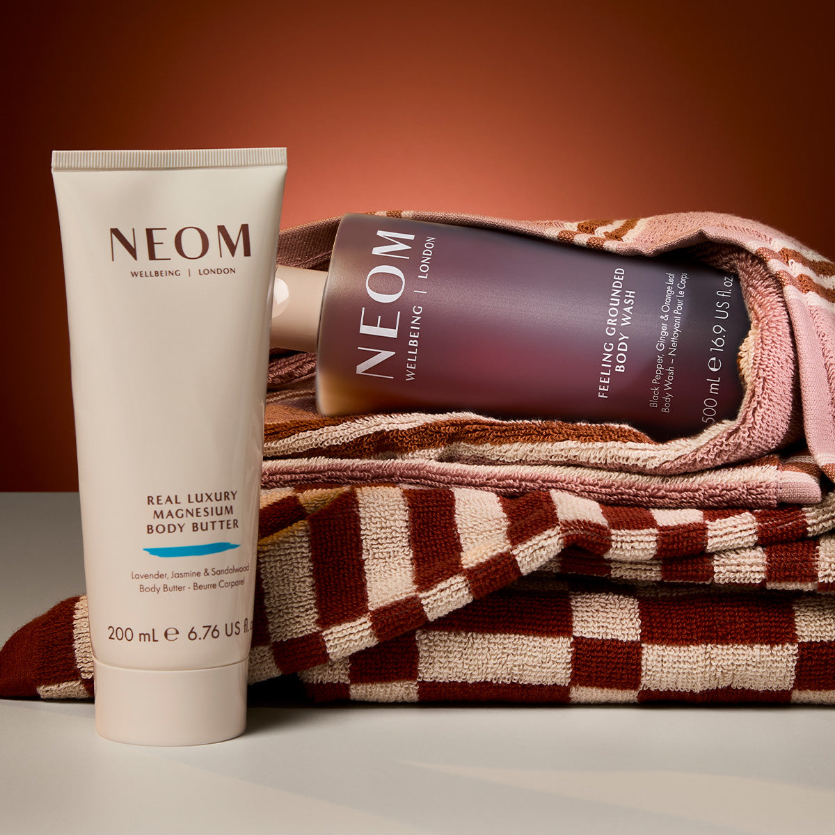 “NEOM Real Luxury Creamy Body Wash and magnesium body butter bottle resting on soft, textured fabric with warm light.