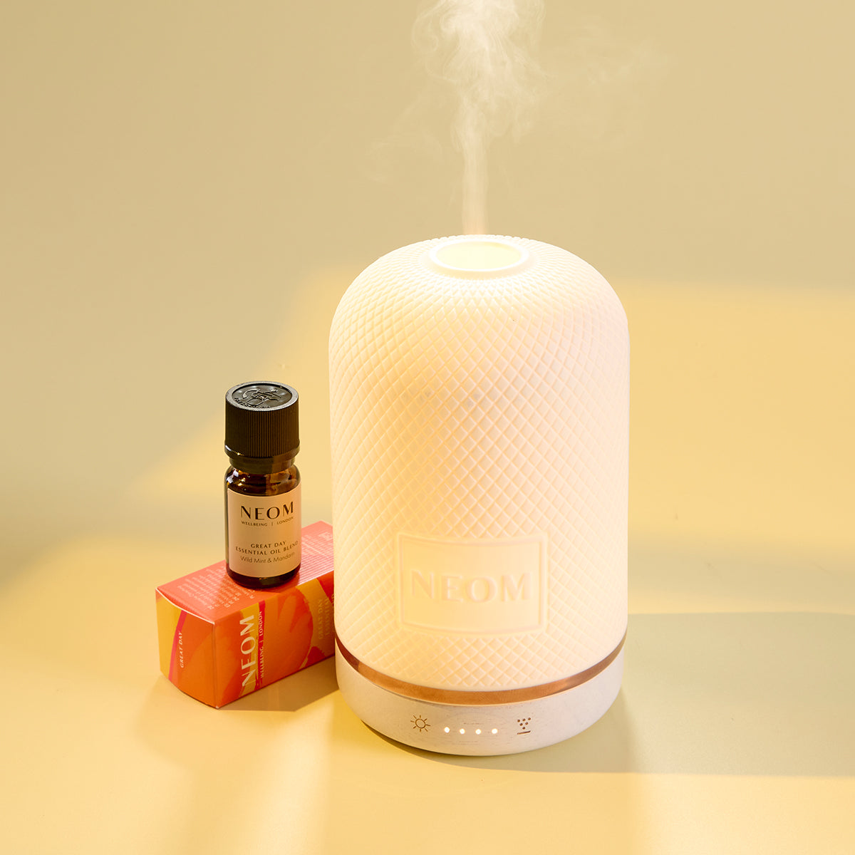White pod diffuser emitting mist with a bottle labelled 'Neom' on a light background