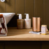 NEOM pod mini+ in rose gold, essential oil blend, hand wash and hand lotion in a a bathroom beside a sink