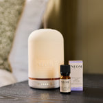 NEOM electric pod diffuser and essential oil bottles on a table with a blurred background