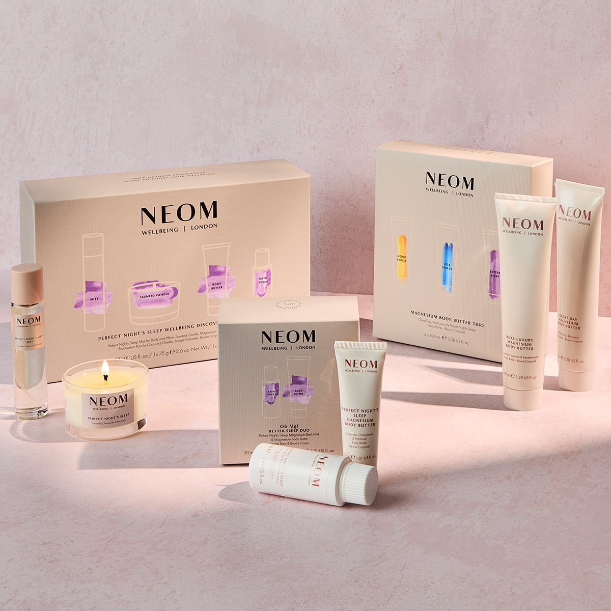 NEOM products including bottles, a candle, sleep mist and boxes on a light pink background