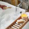 Person holding a NEOM product over a bathtub with a candle and soap on a tray.
