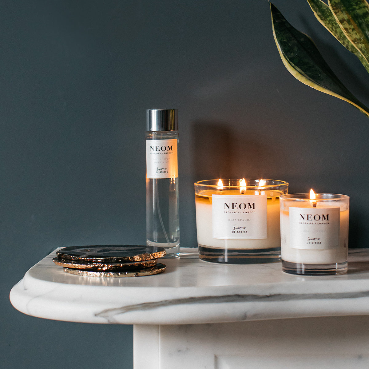 NEOM products including a room spray and two candles on a marble surface with a dark background.