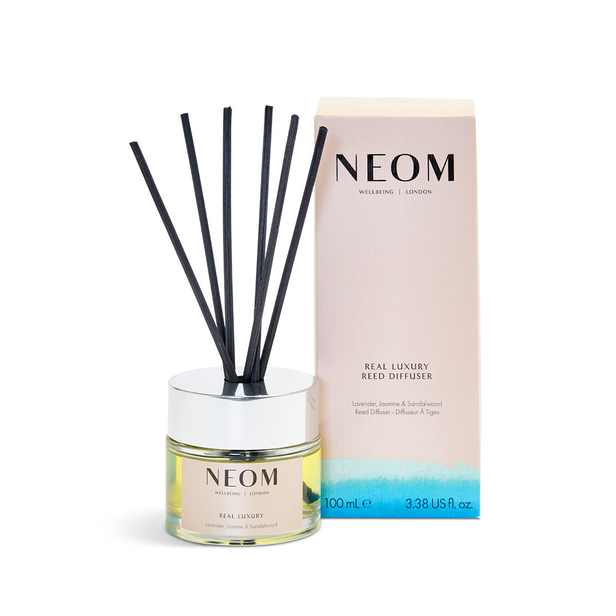 NEOM Real Luxury Reed Diffuser with black reeds and a pink and blue box in the background.