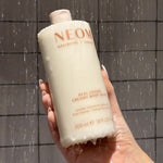 NEOM real luxury creamy body wash being held in the shower by a person