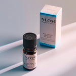 NEOM Real Luxury essential oil blend bottle standing beside its product box on a softly lit surface.
