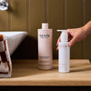 NEOM Super Shower Power Body Cleanser and Energy Burst Multi-Mineral Body Milk on a wooden bathroom shelf beside a sink.