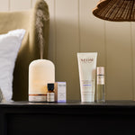 NEOM pod, essential oil blend, magnesium body butter and sleep mist on a bedside table