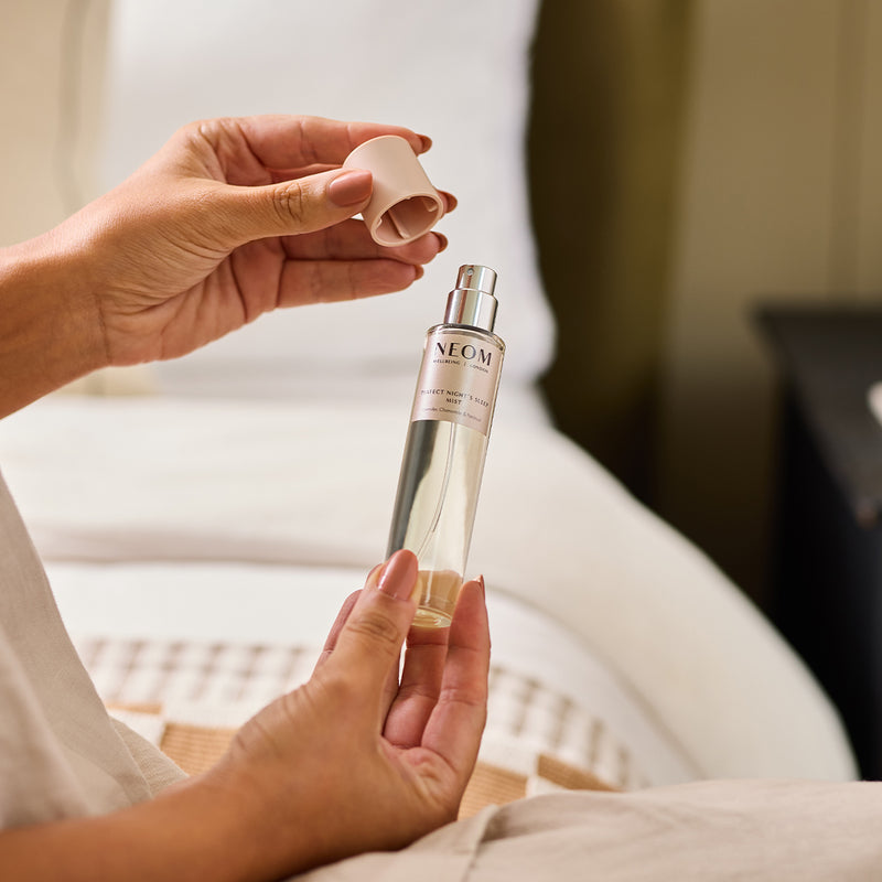 A person holding NEOM perfect night's sleep mist in a bedroom