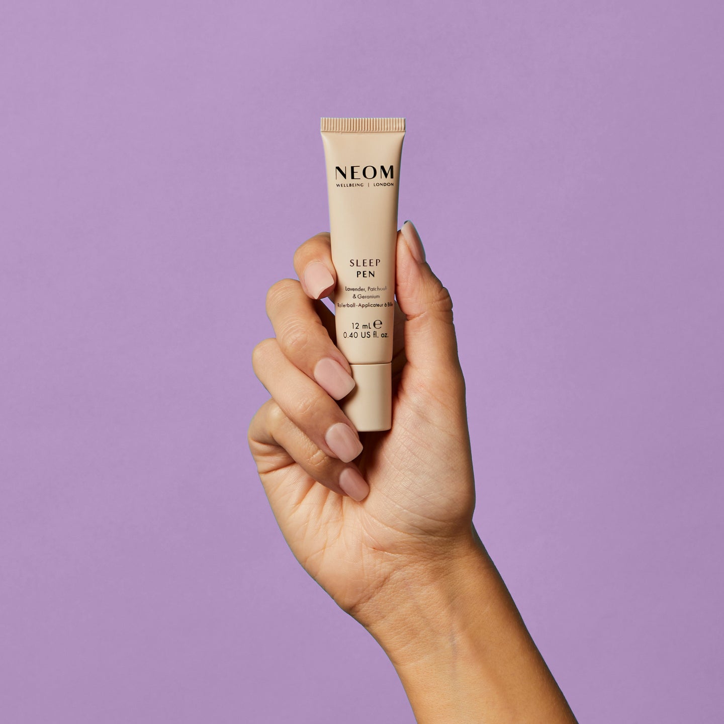 Hand holding a NEOM Sleep Pen against a purple background