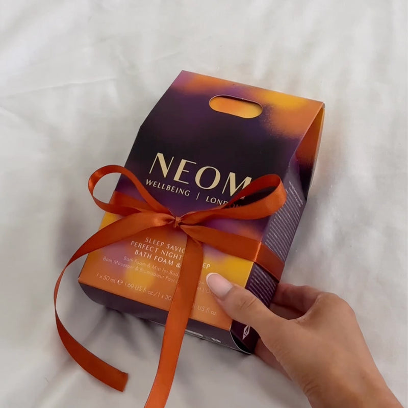 NEOM Sleep Saviours Perfect Night’s Sleep gift set with orange ribbon on white bedding.
