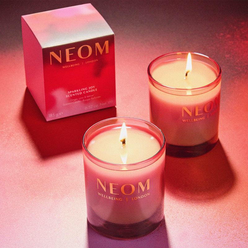 Two NEOM candles with a red box on a pink background