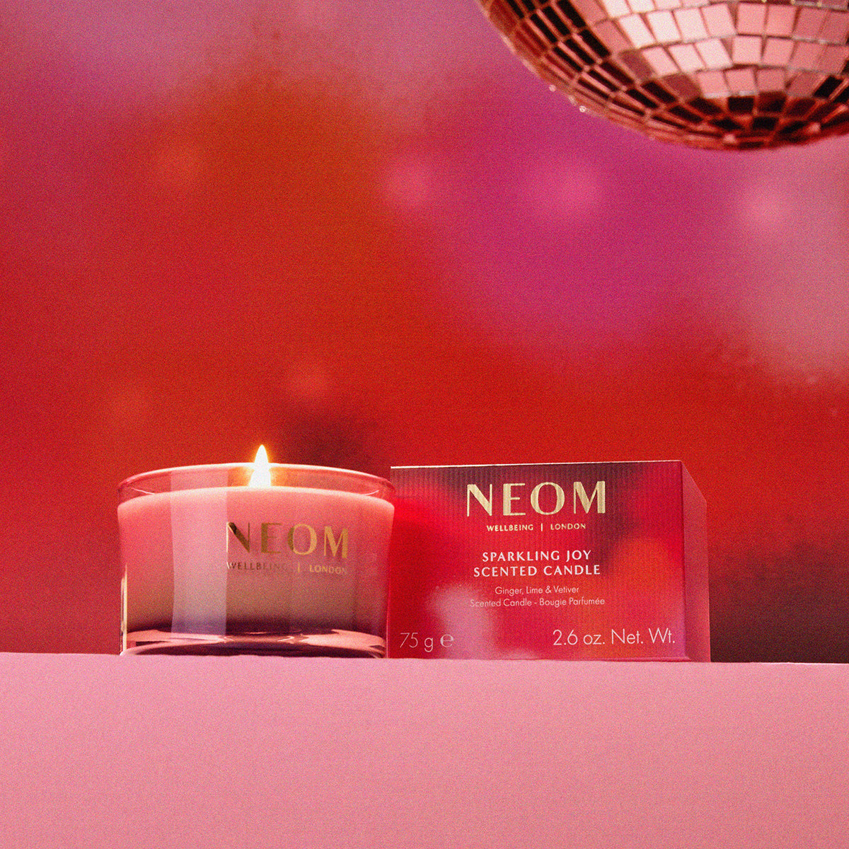 NEOM scented candle and packaging on a pink background with disco ball