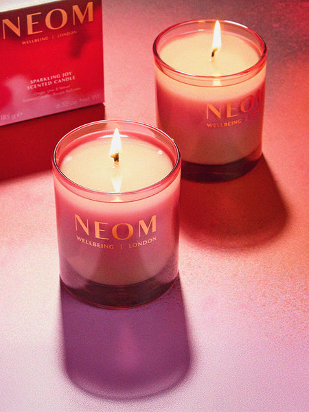 Two NEOM Sparkling Joy candles on a pink background with a box in the corner.