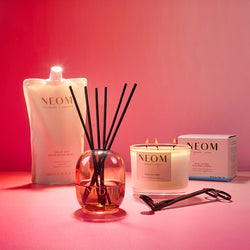 NEOM subscription products including a candle, reed diffuser, and hand wash refill on a pink background