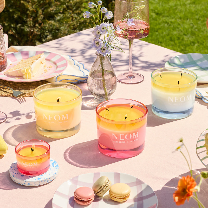 Neom candles on a table with macarons and flowers outdoors
