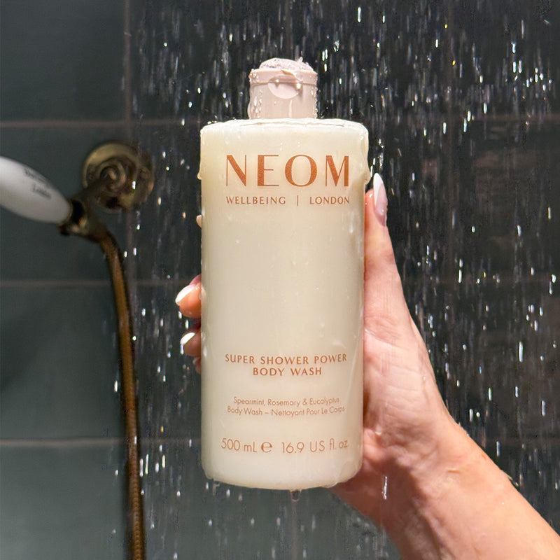 NEOM super shower power body wash in the shower being held by a person