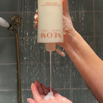 NEOM super shower power body wash upside down being squeezed into a persons hands in the shower