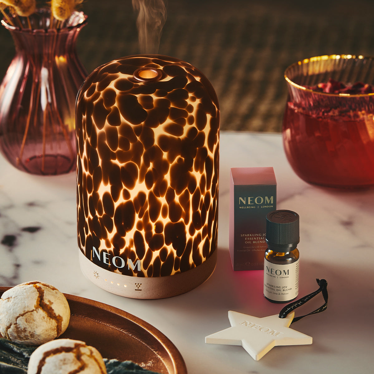 NEOM Tortoiseshell pod diffuser on a table with a NEOM essential oil blend and decorative items.