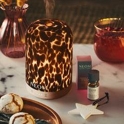 NEOM electric pod diffuser on a table with NEOM products and decorative items.