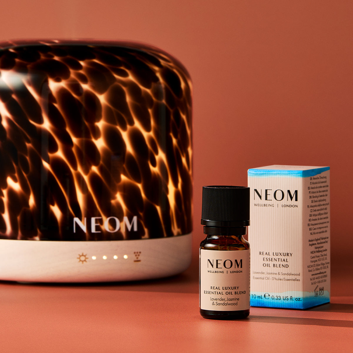 NEOM diffuser, essential oil blend bottle, and packaging on a warm brown background
