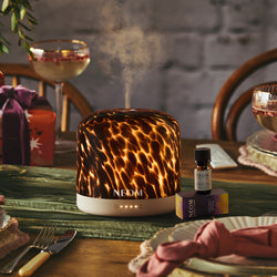 Leopard print NEOM electric pod diffuser on a table with drinks and a stone wall background