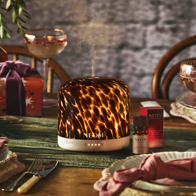 Tortoiseshell print NEOM diffuser on a table with drinks and essential oil blend in the background