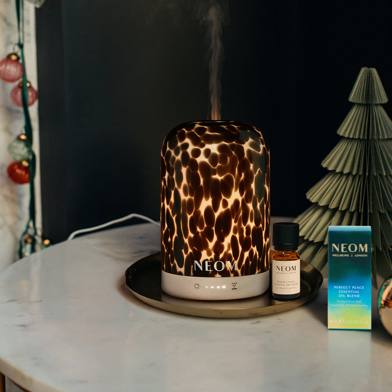 Tortoiseshell print NEOM pod diffuser on a marble surface with an essential oil bottle and box in the background.