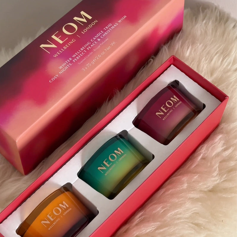 NEOM Winter Wellbeing Candle Trio gift set with three colourful candles in red box on soft fur surface