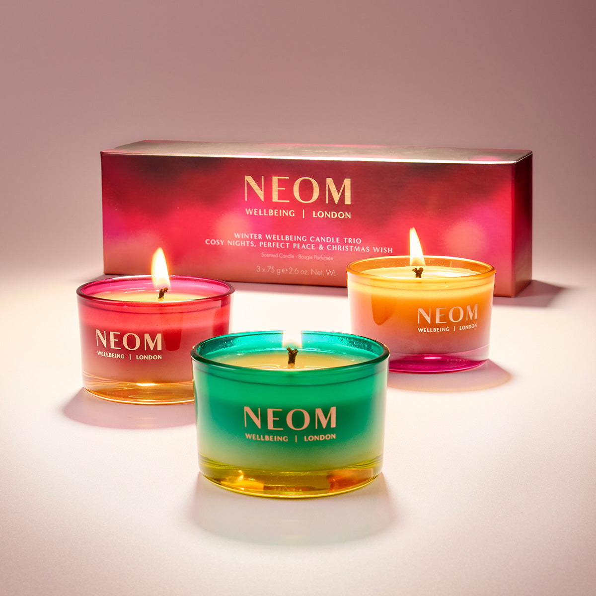 Three NEOM candles with a box in the background on a light surface.