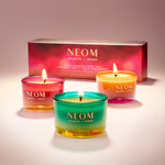 Three NEOM candles with a box in the background on a light surface.