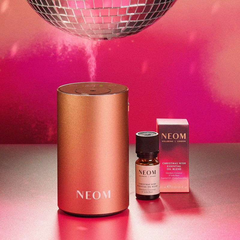 NEOM diffuser and essential oil blend on a reflective surface with a pink background