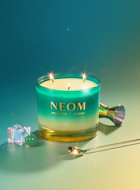 NEOM Perfect Peace Scented Candle with gradient colours on a blue and green background