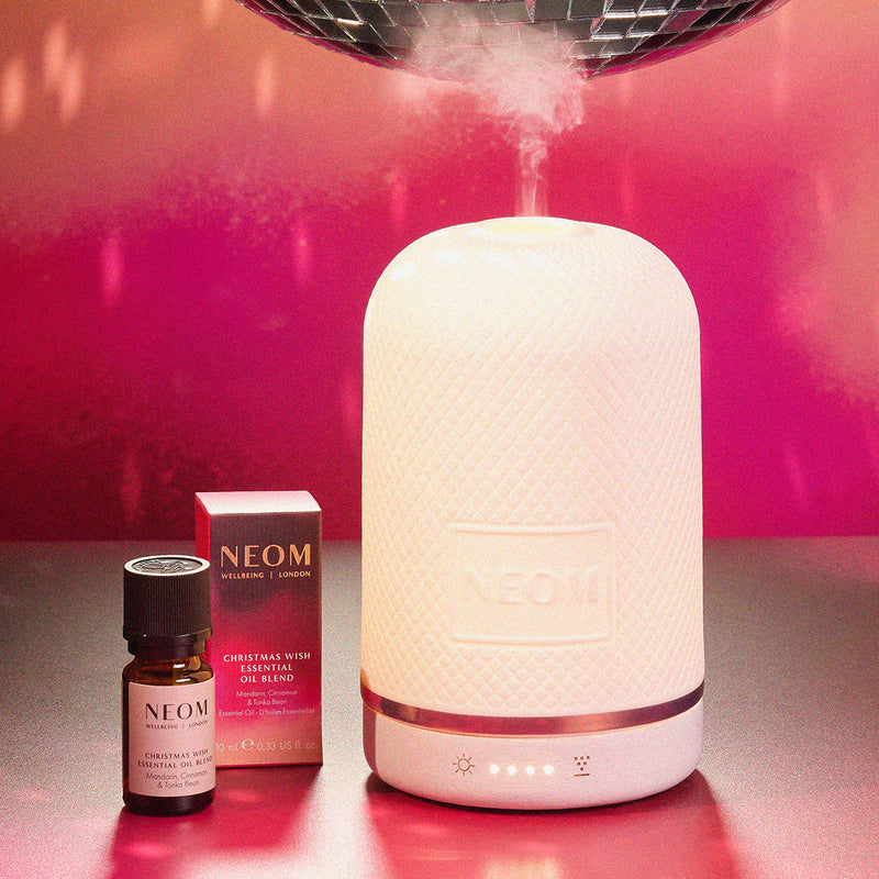 Neom diffuser and essential oil bottle on a pink background