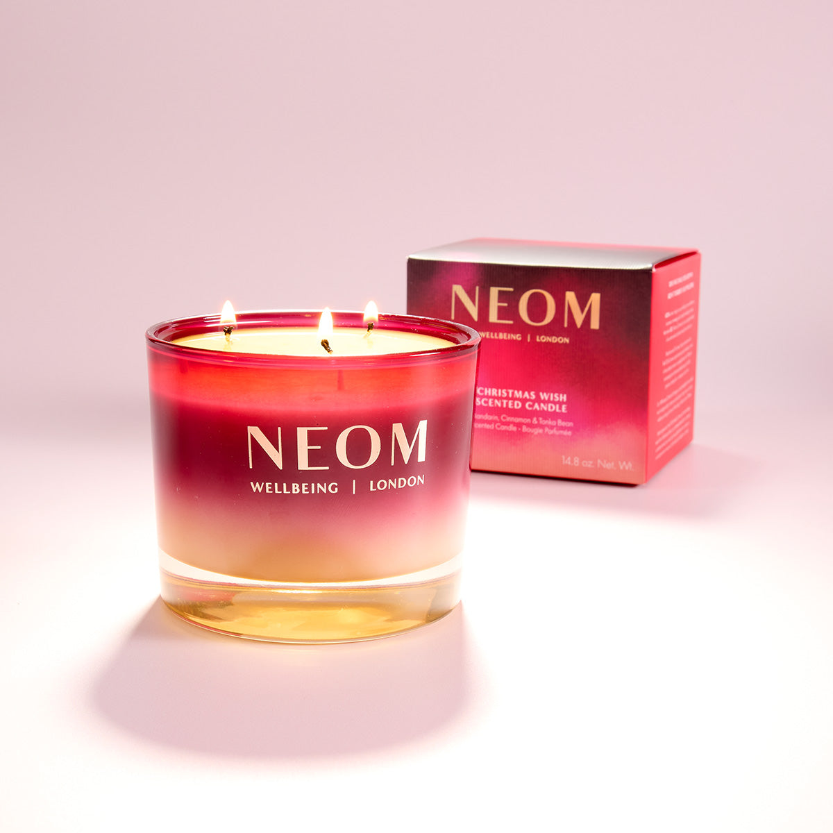 NEOM candle with a matching box on a light pink background