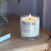 NEOM happiness 1 wick candle lit on a table with a book 